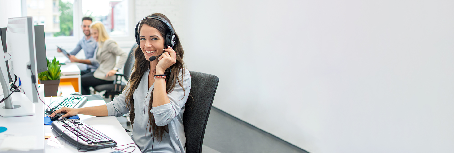 Service Frau mit Headset sitzt in einem Büro und lächelt in die Kamera