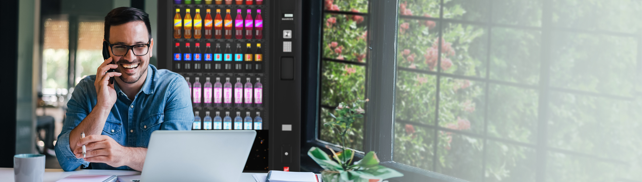 Kaltgetränke Mann mit Brille sitzt am Laptop und telefoniert, im Hintergrund ist ein Kaltgetränkeautomat von Sielaff zu sehen.